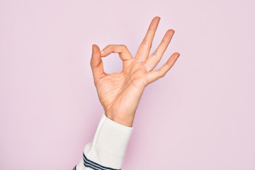 Hand of caucasian young man showing fingers over isolated pink background gesturing approval expression doing okay symbol with fingers