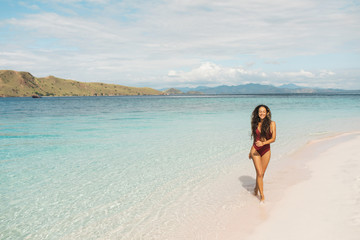 Happy woman in red swimsuit walking by amazing paradise tropical beach with nobody around. Laugh, smile and enjoy summer Vacations.