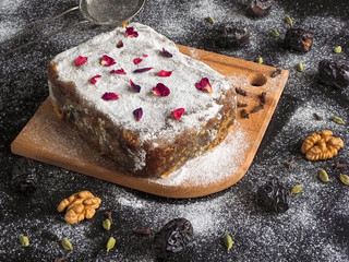Homemade brownie cake with dates and nuts sprinkled with icing sugar on a dark background