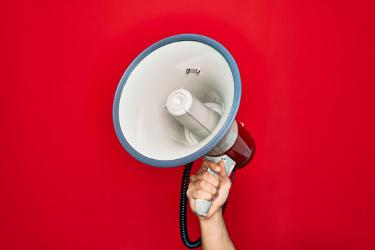Beautiful hand of man holding megaphone over isolated red background