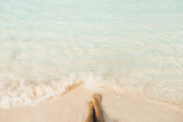 Woman legs barefoot on paradise beach closeup. Clear transparent water splashing on feet. Summer vacations concept, background with empty place for sign.