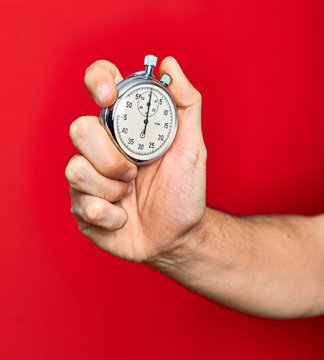 Beautiful hand of man holding stopwatch doing countdown over isolated red background