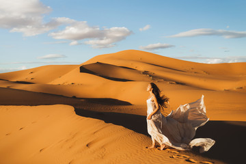 Woman in amazing silk wedding dress with fantastic view of Sahara desert sand dunes in sunset...