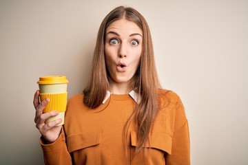 Young beautiful redhead woman drinking cup of coffee over isolated white background scared in shock with a surprise face, afraid and excited with fear expression