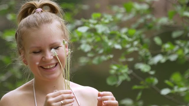 Beautiful attractive girl in a swimsuit in nature in a good mood admires and blows on a dandelion. Green around. Close up
