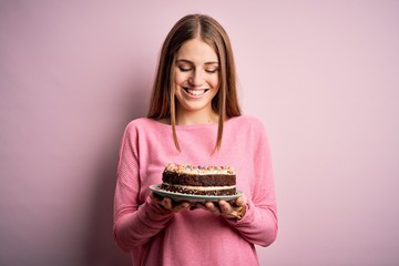 Young beautiful redhead woman holding birthday cake over isolated pink background with a happy face standing and smiling with a confident smile showing teeth