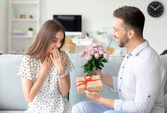 Man giving bouquet of flowers and gift to his girlfriend at home