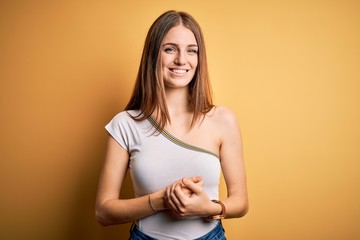 Obraz premium Young beautiful redhead woman wearing casual t-shirt over isolated yellow background with hands together and crossed fingers smiling relaxed and cheerful. Success and optimistic