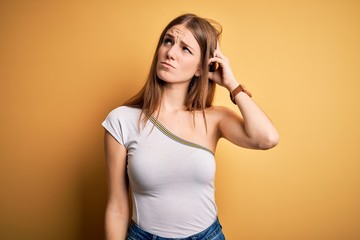 Young beautiful redhead woman wearing casual t-shirt over isolated yellow background confuse and...
