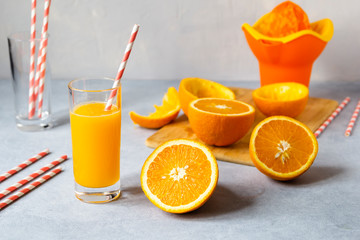 Tall glass of tasty freshly squeezed orange juice standing on table on hot summer day with halved fresh orange.