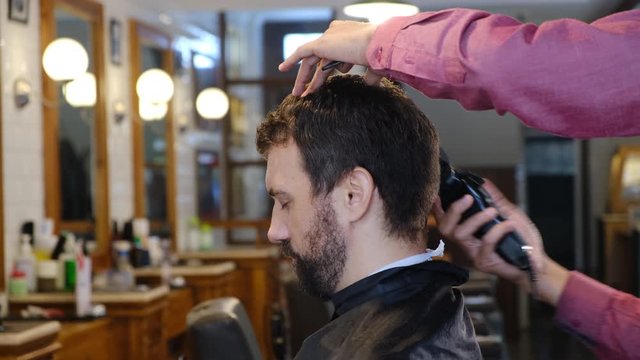 Young man getting hairstyling and haircutting in a barber shop or hair salon. Master cuts hair of men in the barbershop