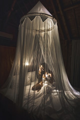 Romantic evening for woman in dark bedroom with lamp light. Covered with beautiful white canopy and sitting on bed. Asian style. © Oleg Breslavtsev