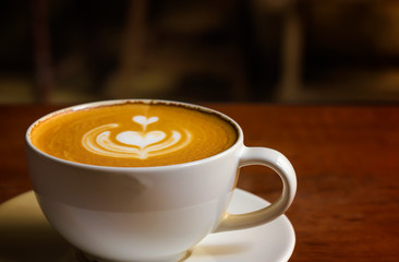 White cup of cappuccino with latte art on wooden background at coffee cafe.