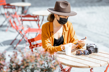 Young woman in facial mask sitting on the cafe terrace alone. Concept of social distancing and new social rules after coronavirus pandemic.