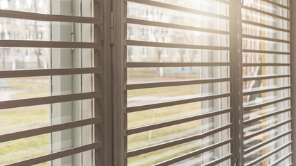 shutters hanging on plastic window against street with green grass and bight sunlight