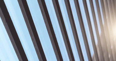 diagonal black shutters planks against blue sky and bright sunlight reflection