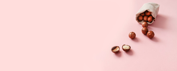 Top view of organic macadamia nuts dropped from burlap sack and place for text on pink background