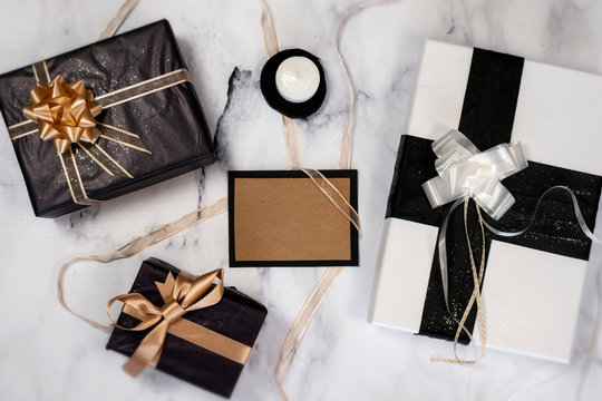 Top view of empty card with gifts and presents and a little candle over white and black marble. All in black, white and gold colors.