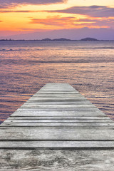 Obraz na płótnie Canvas Sunset at sea and old wooden bridgeมPerspective view of wooden pier on the sea at sunset with perfectly specular reflection,wooden retro deck and sunrise or sunset sky/ Summer holidays background.