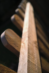 Top detail of a brown wood picket fence, with rounded tops to the posts in sunlight.