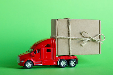 Red toy car truck delivers a parcel in a craft cardboard box on a pastel green background. Delivery...