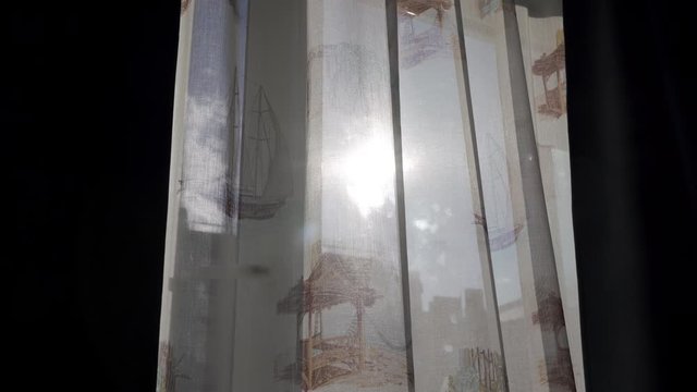 Living room with curtains moved by the wind on draped window, sun shining through the curtain.
