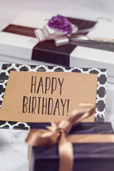 Happy Birthday card with gifts and presents over white marble table, black, white, violet and gold colors.