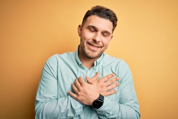 Young business man with blue eyes wearing elegant green shirt over yellow background smiling with...