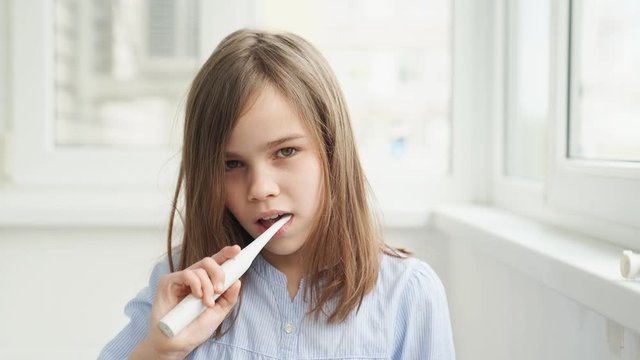 Sleepy girl cleans teeth electric toothbrush