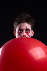 Joven disfrazado de payaso con un globo rojo - obrazy, fototapety, plakaty