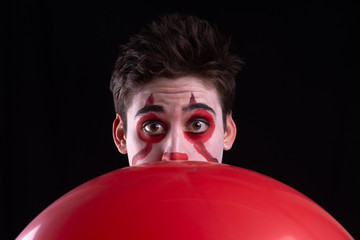 Joven disfrazado de payaso con un globo rojo