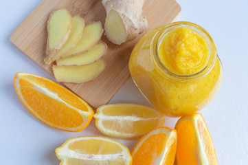 Jar of orange and lemon jam with honey and ginger on a cutting board and slices of lemon and orange