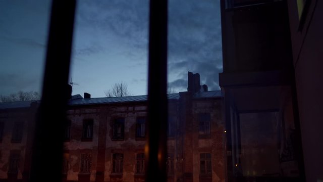 View from the balcony window of an apartment at dusk, old brick building and dark sky with clouds.