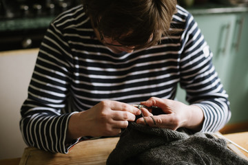 Close up photo of woman's hands knitting on grey yarn on wooden background. Top view