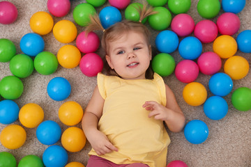 Fototapeta na wymiar Cute little child playing with balls on floor, top view