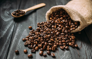 Jute bag with spread coffee beans on wooden table.