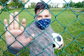 Kid with a protective mask and ball on a children's playground, football, forbidden game