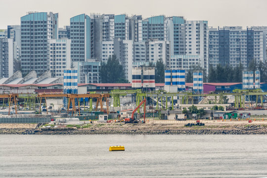 Backhoes and other land moving machinery perform land reclamation and ground improvement works at construction site of new public housing apartments on waterfront of Johor strait in Singapore.