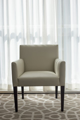 A white leather armchair with wooden legs stands near the window, vertical orientation