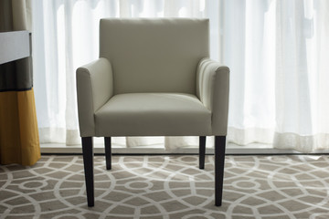 A white leather armchair with wooden legs stands near the window