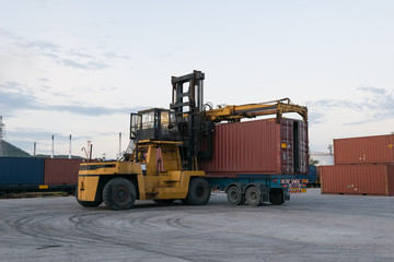 Forklift is loading container box to truck at train station near petrochemical plant in the evening