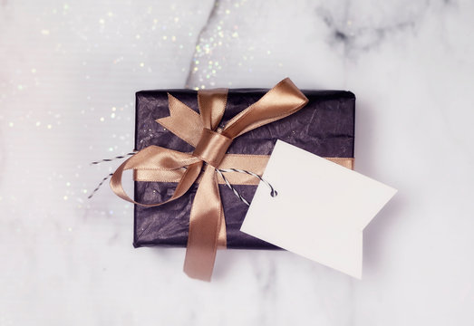 Black Gift With Gold Bow And Empty white Card on a white and black marble table with a bit of glitter.