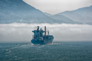 Lonely container carrier ship sailing bound in thick sea fog in restricted visibility condition.