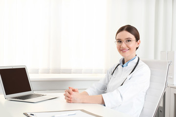 Portrait of young female doctor in white coat at workplace