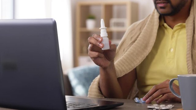 healthcare, technology and people concept - sick indian man in blanket with thermometer having video call on laptop computer at home