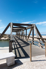 wooden bridge crossing a small river linking a path to a boardwalk. Praia da Areia Branca, near Lourinha, Portugal