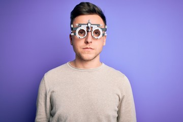 Young handsome caucasian man wearing optometrical glasses over purple background with serious expression on face. Simple and natural looking at the camera.