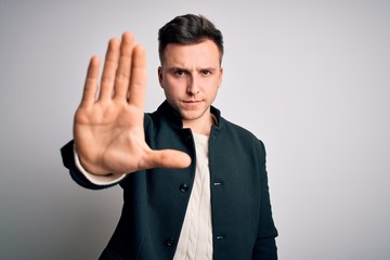 Young handsome business mas wearing elegant winter coat standing over isolated background doing stop sing with palm of the hand. Warning expression with negative and serious gesture on the face.