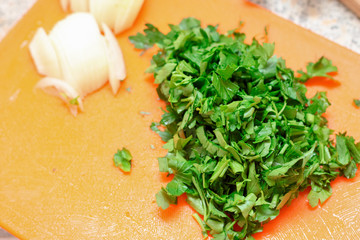 Cooking at home. Sliced ​​parsley and onions on a board.