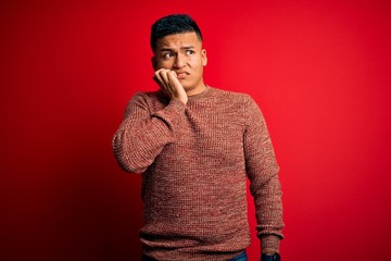 Young handsome latin man wearing casual sweater standing over red background looking stressed and...